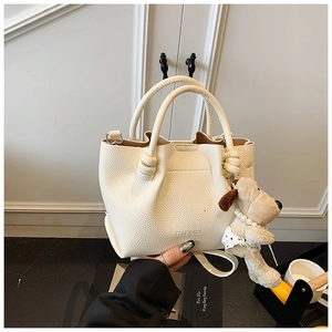 Detail of off-white lychee texture bucket bag with knot handle and plush puppy pendant