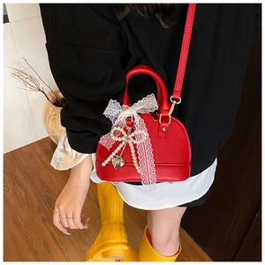 Detail of red shell-shaped crossbody bag with white lace bow and pearl heart charm