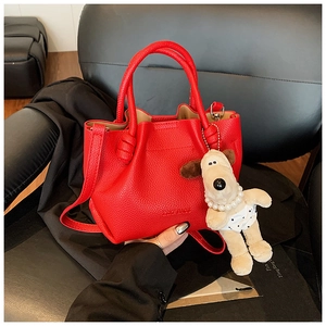 Detail of red lychee textured bucket bag featuring a cute beige puppy charm and strap
