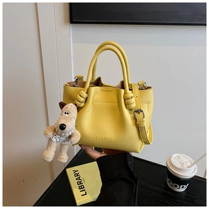 Detail of yellow lychee leather bucket bag with plush dog charm and pearl necklace