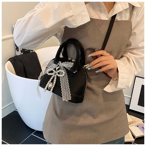 Detail of black lychee leather bag with white lace bow and pearl heart charm