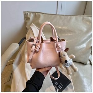 Detail of pink lychee pattern bucket bag with soft plush puppy pendant and logo