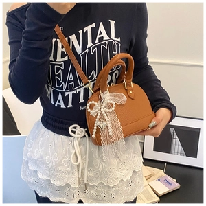 Close-up of brown litchi pattern shell bag with white lace pearl bow and heart charm