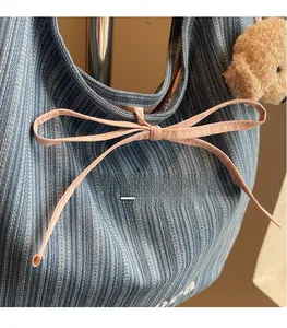 Detail of blue striped tote bag featuring pink bow and plush bear charm accessory