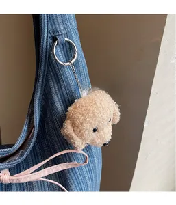 Close-up of a fluffy beige dog plush pendant on a blue denim shoulder bag handle