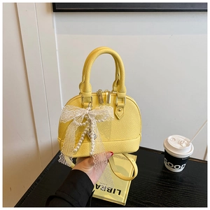 Detail of yellow shell bag with lychee texture leather and white lace bow accessory