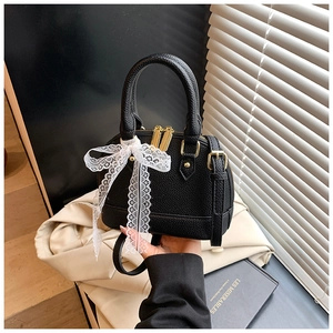Detail of black lychee grain leather mini shell bag with a white lace bow and gold zippers