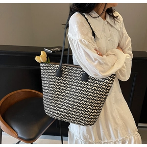 Close-up of woven straw tote bag with black and white chevron pattern and long handles