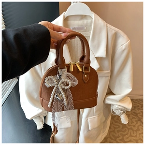 Close-up of brown litchi pattern shell bag with white lace bow and pearl heart charm