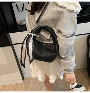 Detail of black lychee leather bucket bag featuring a silk scarf on handle and silver lock