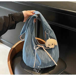 Detail of blue corduroy tote bag featuring white Aurora lettering and plush puppy charm