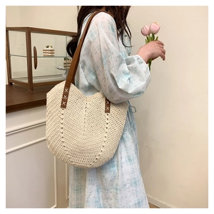 Close-up of woven straw tote bag featuring brown leather straps and detailed stitching