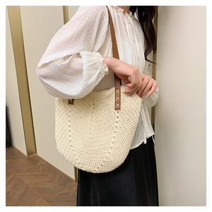 Detail of hand-woven straw shoulder bag with brown leather straps and cross-stitch accents