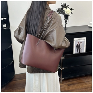 Close-up of a burgundy leather tote bag with silver chain straps worn by a model