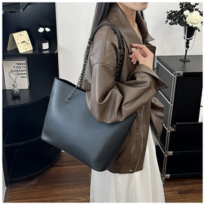 Fashionable large black tote bag with metal chain strap shown in a lifestyle street setting