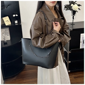 Detail of a large black faux leather tote bag with dark grey chain strap on a model