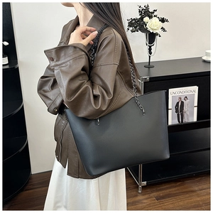 Detail view of large black leather tote bag with chain strap styled on model shoulder