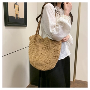 Detail of woven straw tote bag with brown leather straps and cross-stitch reinforcement