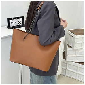 Detail of a large brown tote bag showing smooth faux leather texture and metal chain strap