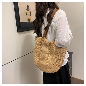 Detail of herringbone woven straw tote bag featuring brown leather straps and X-shape stitching