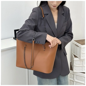 Detail view of brown leather tote bag with stylish metal chain strap on model