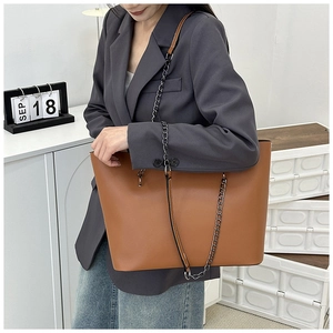 Detail view of caramel brown tote bag with metal chain strap on female model