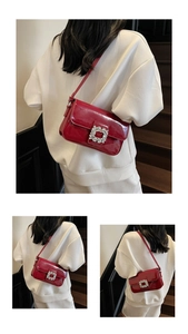 Macro shot of red patent leather shoulder bag featuring a large square rhinestone buckle