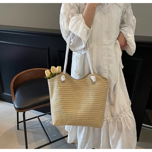 Detail of large straw woven tote bag featuring thick white cotton rope handles and texture
