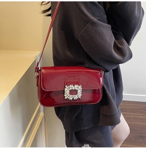 Close-up of deep red patent leather shoulder bag with a square rhinestone buckle detail