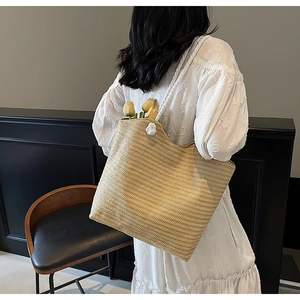 Detail of a large woven straw tote bag with white rope handles and decorative pompom charm