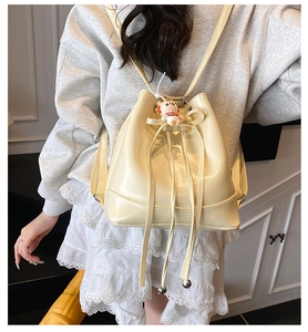 Detail of a creamy leather bucket backpack featuring a drawstring and sweet bow decoration