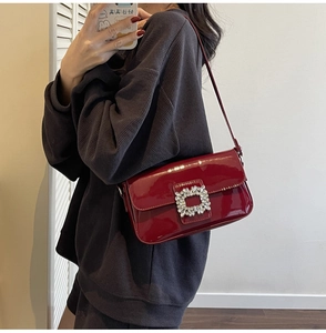 Close-up of a burgundy patent leather underarm bag featuring a luxury crystal buckle