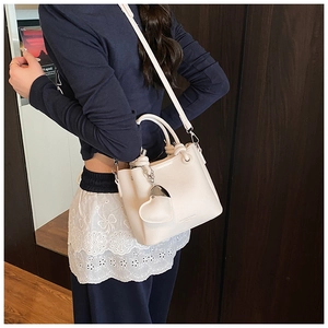 Détail d'un sac seau beige à motif litchi avec un grand pendentif en forme de cœur