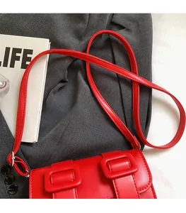 Detail view of bright red leather satchel bag with dual buckle design and adjustable strap