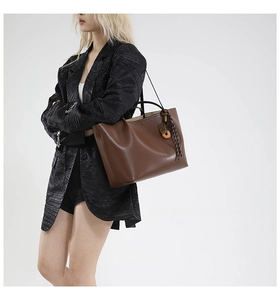 Detail shot of a large brown leather tote bag with unique woven rope and wooden pendant charm