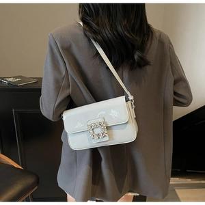 Detail view of square rhinestone buckle on light gray patent leather shoulder bag