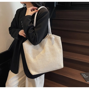Detail of a large straw tote bag featuring thick cotton rope handles with decorative knots