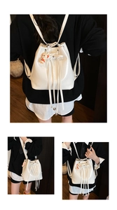 Detailed view of white bucket bag featuring drawstring closure, fringe and rabbit charm