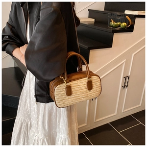Detail of a straw woven handbag with brown leather trim and golden metal hardware