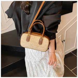Detail of a straw woven handbag with brown leather trim worn by a model in a minimal setting
