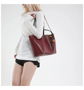 Detail view of large burgundy leather tote bag with elegant tassel charm and shoulder straps