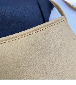 Close-up of beige leather shoulder bag showing pebble texture and silver brand logo