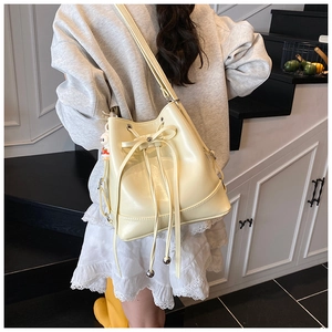 Detail view of cream white bucket bag with drawstring closure and cute plush charm pendant