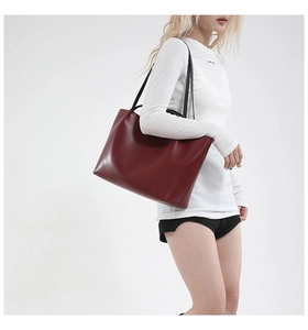 Detail view of large burgundy leather tote bag with black straps worn by a model