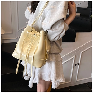 Detail of creamy yellow bucket bag with drawstring closure, ribbon bow and metal charms