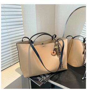 Close-up of cream tote bag with black handles and decorative pendant in soft indoor lighting