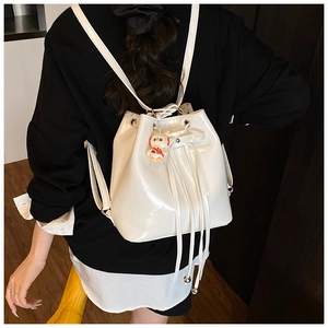 Detailed view of white patent leather bucket bag with tassel drawstring and plush charm