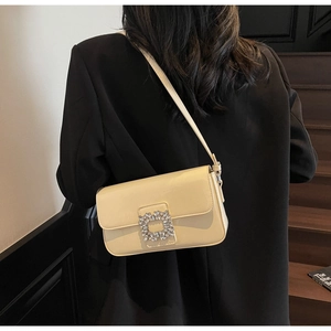 Detail view of a cream leather shoulder bag with a sparkling crystal square buckle