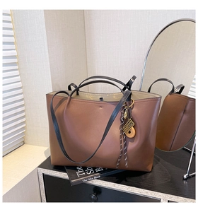 Detail of large brown leather tote with black straps and golden abacus charm