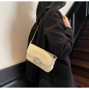 Detail of elegant cream patent leather shoulder bag with sparkling rhinestone buckle